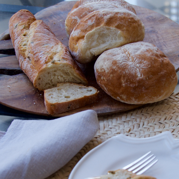 Freshly baked bread loaves on a wooden board with a white napkin and plate.