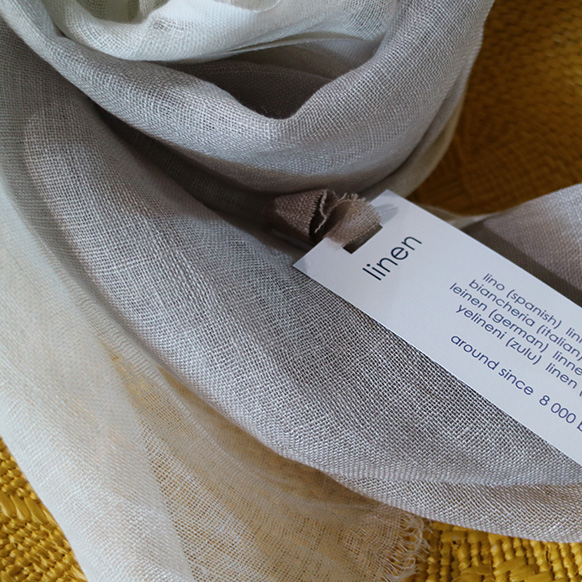 Close-up of beige linen fabric with a tag displaying the word "linen" in multiple languages.