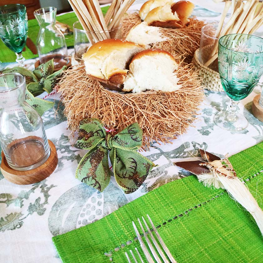Festive table setting with bread, green glasses, and decorative bows on a patterned tablecloth.