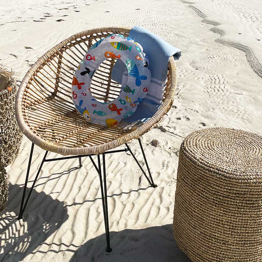 Rattan chair on sandy beach with inflatable ring and towel.