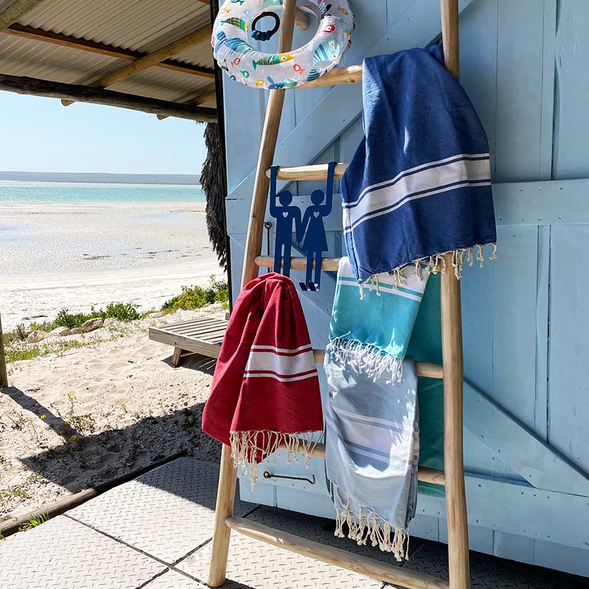 Beach towels hanging on a wooden ladder by a seaside hut.