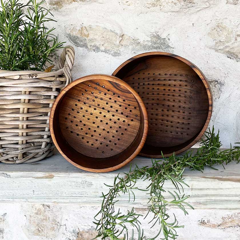 Wooden colanders on shelf with wicker basket and rosemary sprigs.