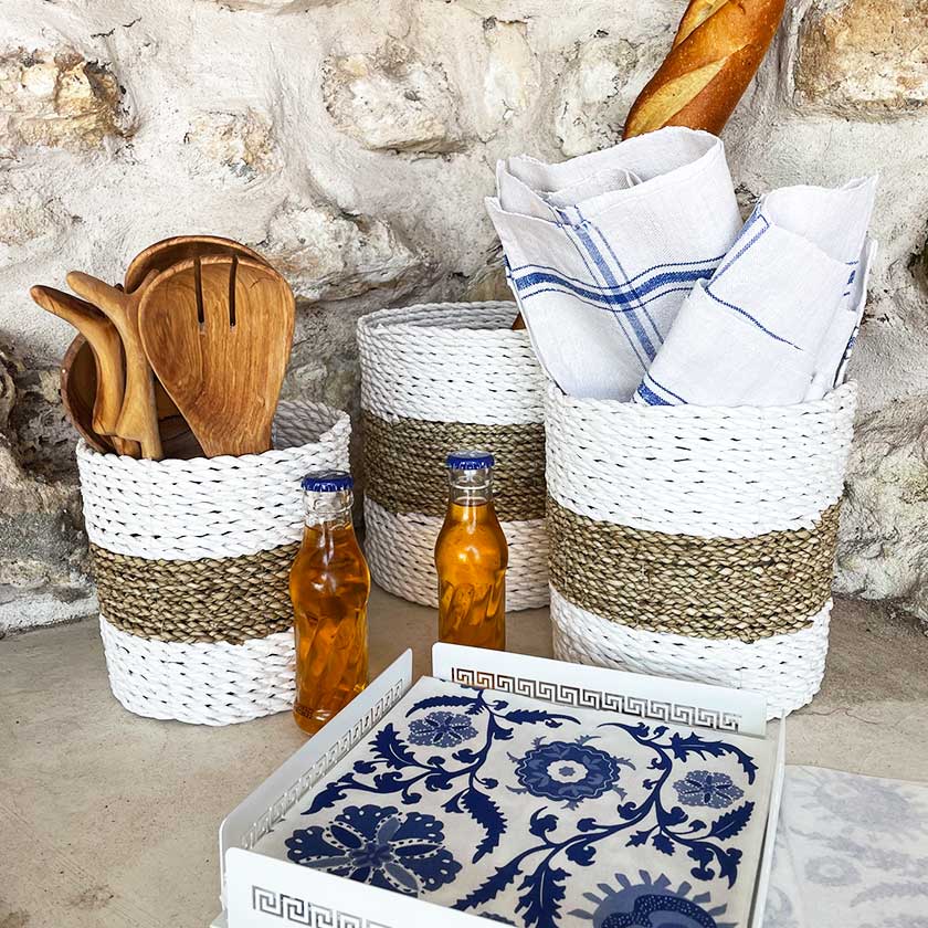 Woven baskets with utensils and napkins, two bottles, and a decorative tray on a stone surface.