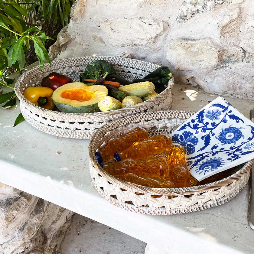 Woven baskets with fresh vegetables and glass bottles on a stone surface.