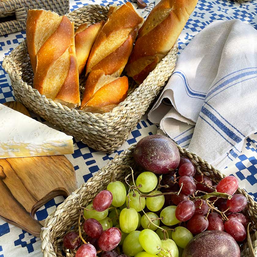Baskets with baguettes, grapes, and cheese on a checkered tablecloth.