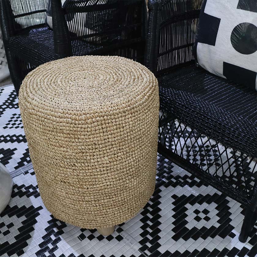 Woven ottoman on black and white patterned rug next to black wicker chairs.