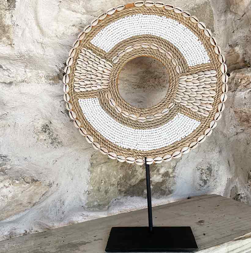 Decorative circular shell ornament on a stand against a stone wall.