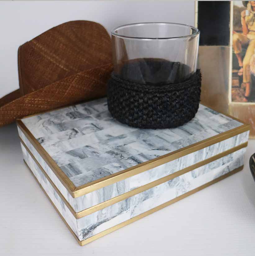Decorative box with glass and woven holder, brown hat in background.