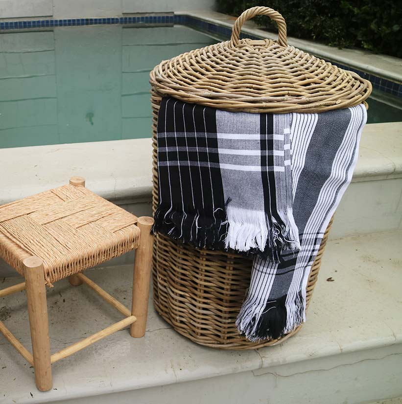 Wicker basket with plaid blanket by poolside, next to a small wooden stool.